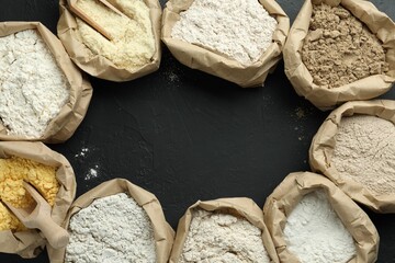Frame of different flour types in paper bags on black table, flat lay. Space for text