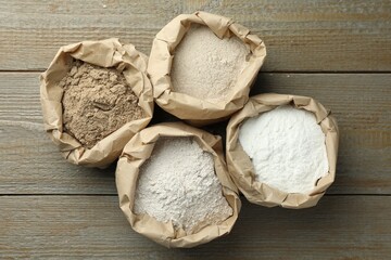 Different types of flour in paper bags on wooden table, flat lay