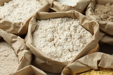 Different types of flour in paper bags on white table, closeup