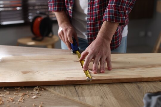 Man measuring wooden plank with tape indoors, closeup