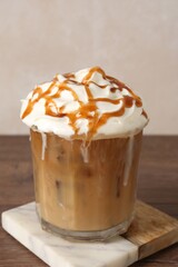 Tasty iced coffee with whipped cream and syrup on wooden table, closeup