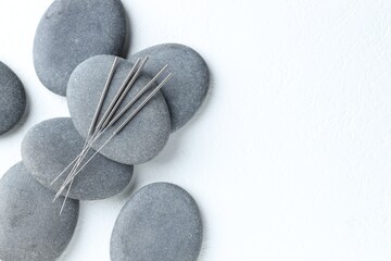 Acupuncture needles and spa stones on white background, flat lay. Space for text