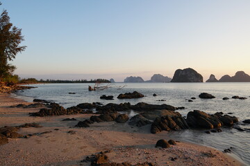 Serene Beach View at Dusk with Rocky Shoreline and Silhouetted Mountains in the Background