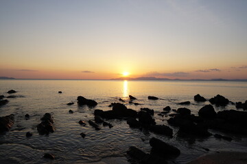 Fototapeta premium Serene Sunset Over Calm Waters with Silhouetted Rocks and Gentle Waves at Dusk