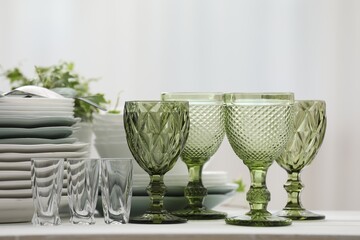 Clean glasses, plates, cutlery and green houseplant on white table indoors
