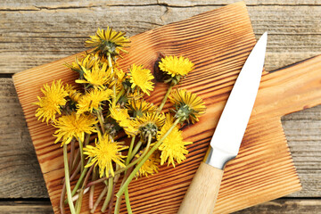 Dandelion flowers, knife and cutting board on wooden table, top view