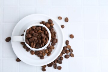 Aromatic coffee beans, cup and saucer on white tiled table, flat lay. Space for text