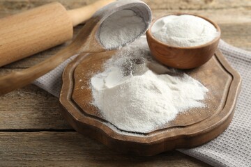 Wheat flour, spoon and rolling pin on wooden table, closeup