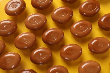Many tasty caramel candies on yellow background, flat lay