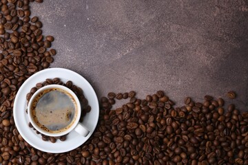 Aromatic coffee in cup, saucer and beans on brown textured table, flat lay. Space for text