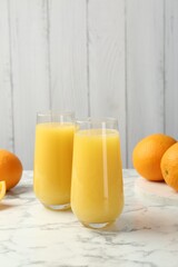 Orange juice in glasses and fresh fruits on white marble table