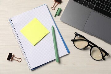 Notebook, sticky note, pen, glasses, binder clips and laptop on wooden table, flat lay