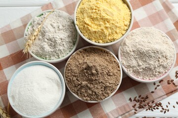 Different types of flour in bowls, spike and flaxseeds on table, flat lay