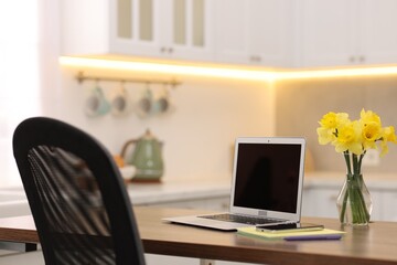 Laptop with blank screen, smartphone, stationery and flowers on wooden table in kitchen. Mockup for design
