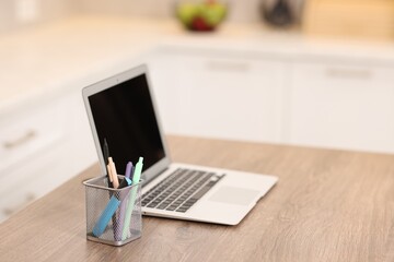 Laptop with blank screen and stationery on wooden table in kitchen, selective focus. Mockup for design