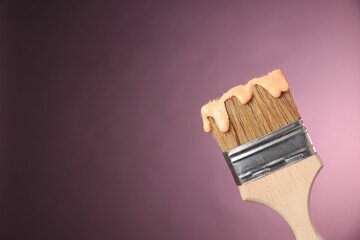 Brush with paint on pink background, closeup. Space for text