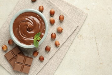 Tasty chocolate spread, pieces, mint and hazelnuts on light table, flat lay. Space for text