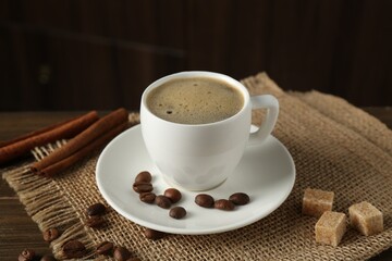 Aromatic coffee in cup, beans, brown sugar and cinnamon on table, closeup