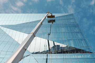 Cleaner worker using a cherry picker to clean a glas facade of a contemporary office building © Jarama