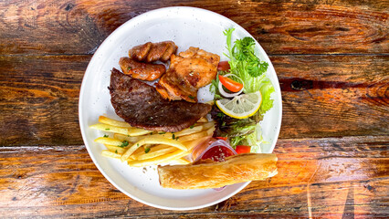 High angle detail of grilled steak with potatoes and salad elegantly arranged on rustic backdrop.