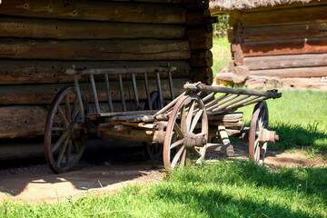  old wooden cart with large wheels standing near a wooden Ukrainian house in the yard