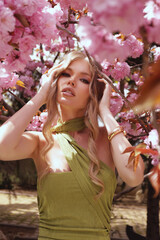 Fototapeta premium beautiful woman with blond hair in elegant dress and accessories posing in blooming sakura garden