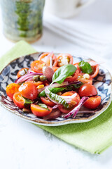 Simple salad with cherry tomatoes, red onion and fresh herbs. Bright wooden background. Close up.	
