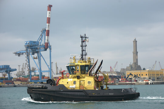Rimorchiatore giallo mTug in operazione nel porto industriale di Genova con la Lanterna sullo sfondo