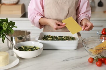 Woman making spinach lasagna at marble table indoors, closeup