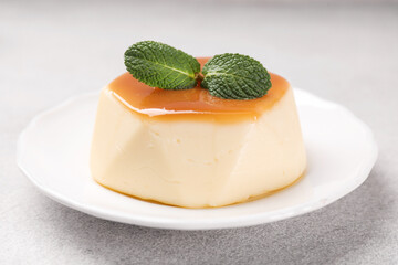 Delicious pudding with caramel sauce and mint on light table, closeup