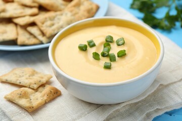Tasty cheese dipping sauce in bowl and crackers on table, closeup
