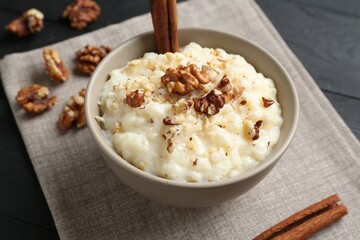Delicious rice pudding with walnuts and cinnamon on black table, closeup