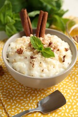 Delicious rice pudding with walnuts, cinnamon, mint and spoon on table, closeup
