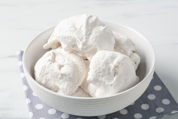 Delicious homemade meringue cookies in bowl on light table, closeup