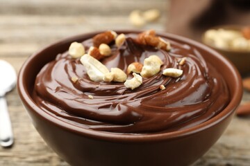 Delicious chocolate pudding with nuts in bowl on wooden table, closeup