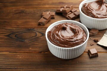 Tasty pudding in bowls and pieces of chocolate on wooden table, space for text