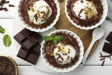Tasty pudding with whipped cream in bowls, pieces of chocolate and spoon on white wooden table, flat lay