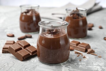 Tasty pudding in glass jars and pieces of chocolate on light grey table, closeup