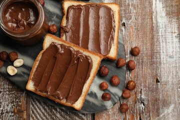 Toasts with tasty chocolate hazelnut spread and nuts on wooden table, flat lay