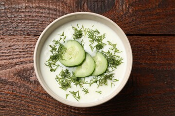 Tasty cucumber soup in bowl on wooden table, top view