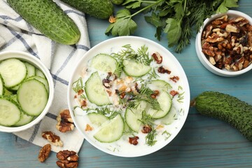 Tasty cucumber soup with dill and nuts in bowl on light blue wooden table, flat lay