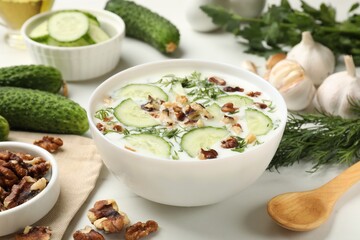 Tasty cucumber soup with dill and nuts in bowl on white table, closeup