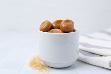 Tasty sweet caramel candies on white tiled table, closeup