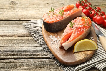 Seafood. Salmon steaks, spices, lemon wedge and tomatoes on wooden table, closeup. Space for text