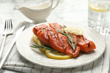 Seafood. Tasty grilled salmon served with cutlery, rosemary and lemon on white table, closeup