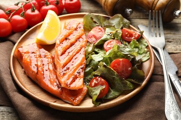Seafood. Tasty grilled salmon served with cutlery, salad and lemon on wooden table, closeup