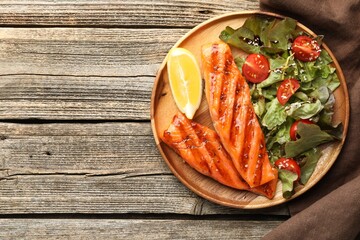 Tasty grilled salmon served with salad and lemon on wooden table, top view. Space for text