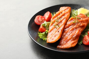 Tasty grilled salmon served with lettuce, tomatoes and lemon on grey table, closeup. Space for text