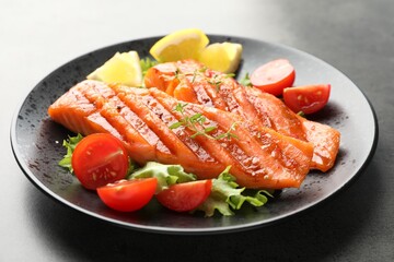 Tasty grilled salmon served with lettuce, tomatoes and lemon on grey table, closeup
