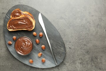 Toasts with tasty chocolate spread and hazelnuts on gray textured table, top view. Space for text